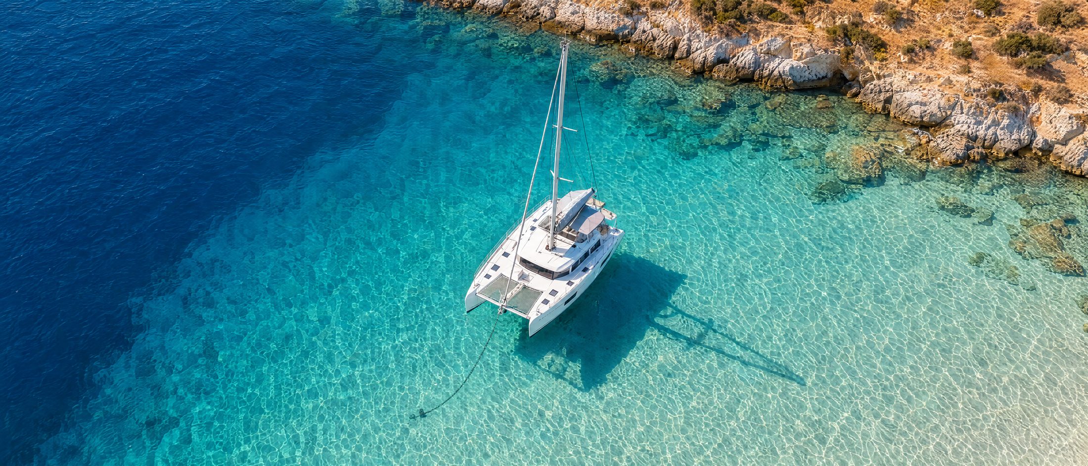 A sailing catamaran at anchor in a turquoise Cycladic bay at golden hour